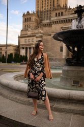 a lady in a black dress with white floral prints and a brown jacket